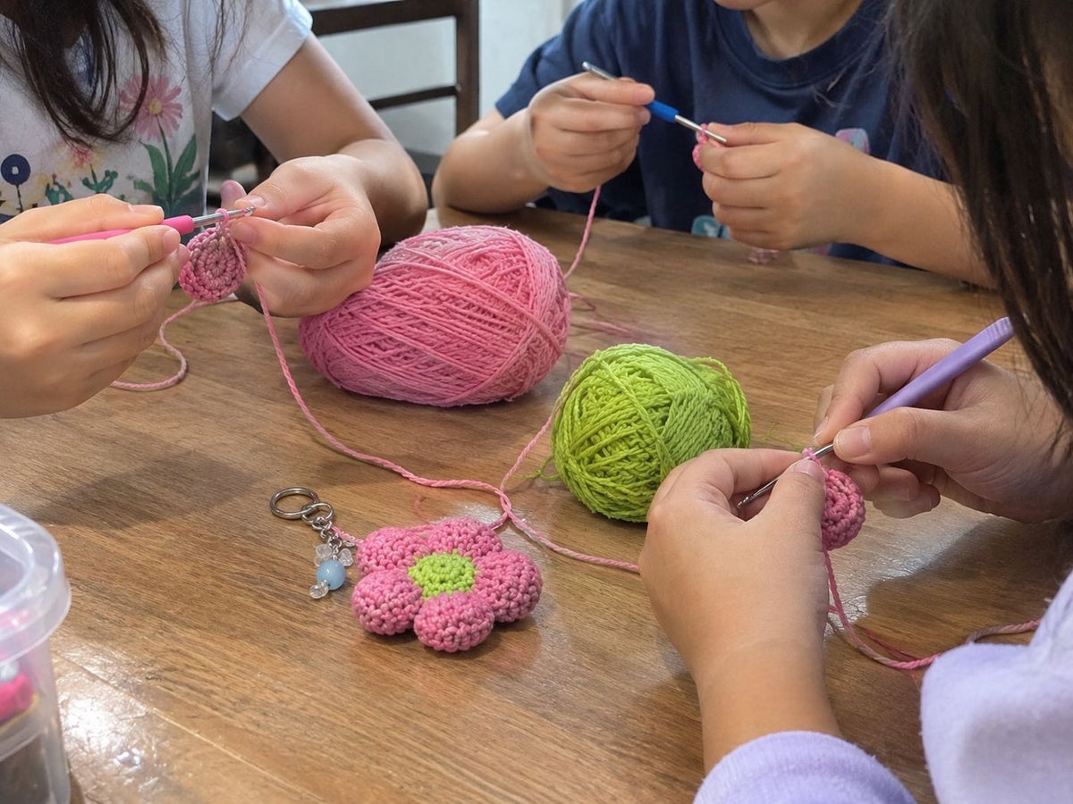 Children crocheting charms together with pink and green yarn, beside a finished pink flower keychain